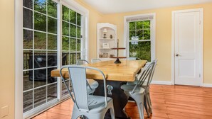 A dining area with a wooden table and metal chairs, large windows, and a door. - Pine Hollow Hideout: Access to Canadarago Lake (Richfield Springs)