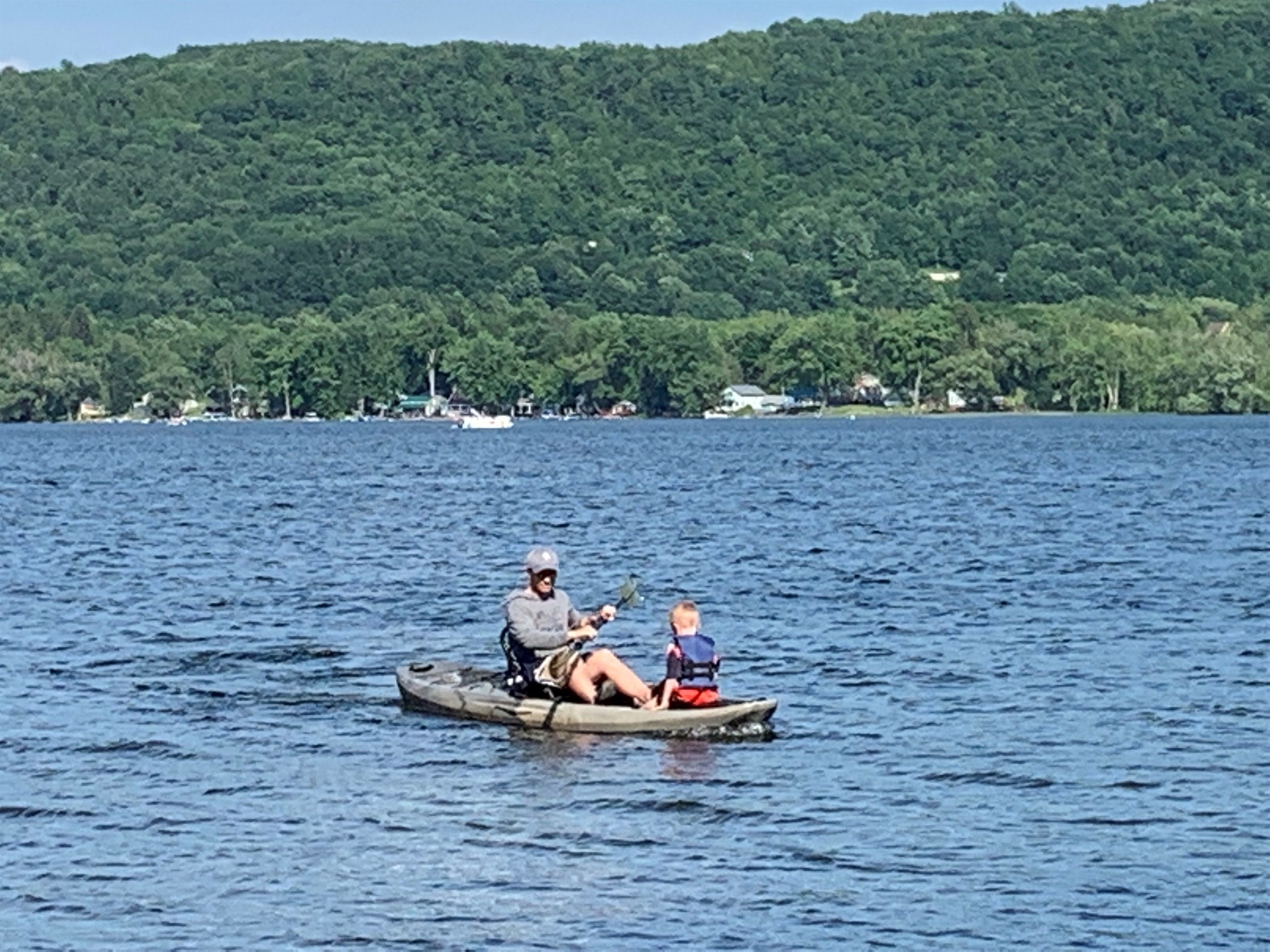 A person in a boat on a body of water with a forested hill in the background.