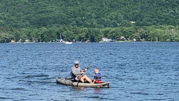 A person in a boat on a body of water with a forested hill in the background.