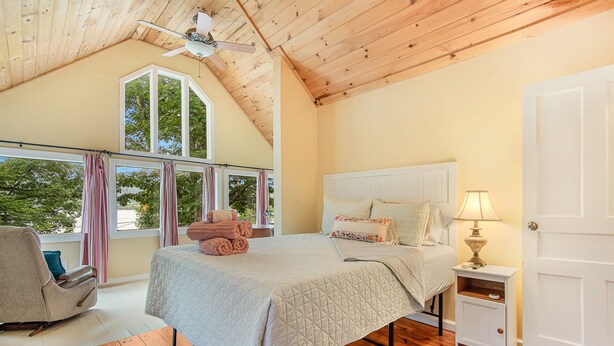 A bedroom with a bed, a nightstand, a chair, a window with curtains, and a ceiling fan. - Pine Hollow Hideout: Access to Canadarago Lake (Richfield Springs)