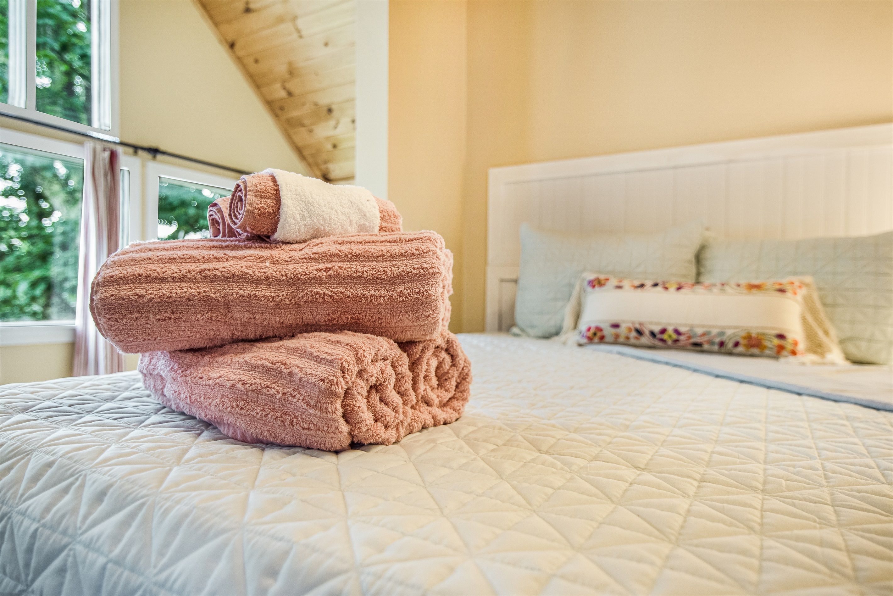 A bed with a quilted bedspread and a stack of folded towels.