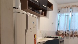 A kitchen with a refrigerator, oven, and a window with curtains. - Apto Agua Marinha (Campos dos Goytacazes)