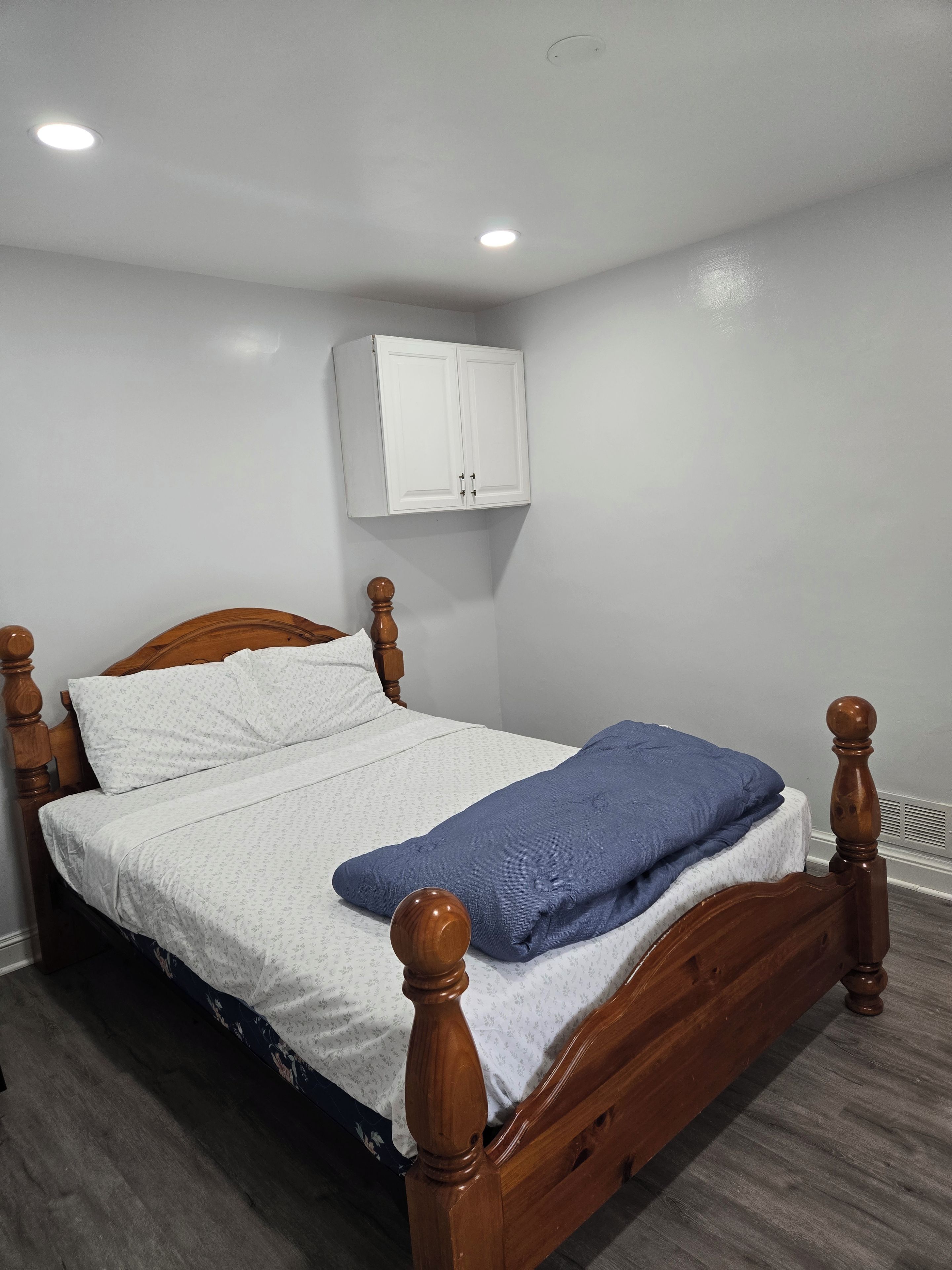 Un dormitorio con una cama de madera, paredes blancas, techo blanco y un armario blanco.