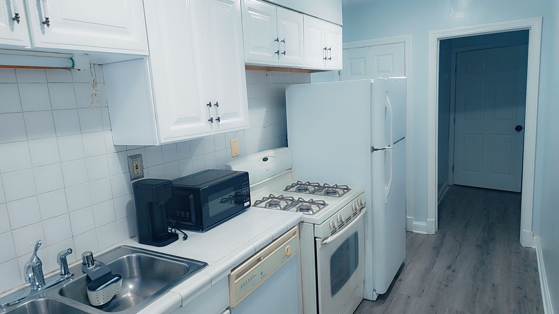 Une cuisine avec des meubles blancs, un four à micro-ondes, une cuisinière et un réfrigérateur.