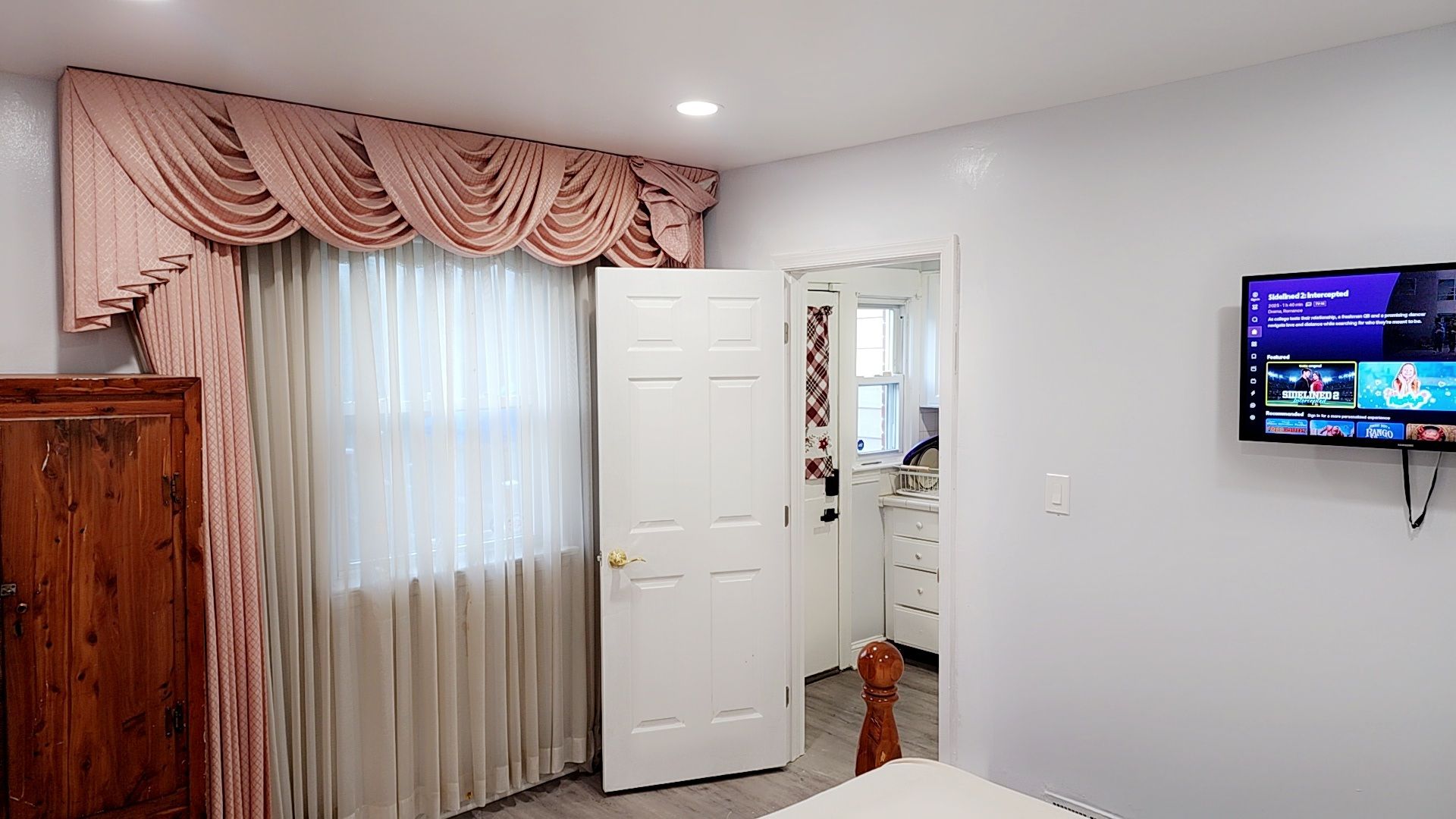 Una habitación con un televisor montado en la pared, una puerta con cortina y un armario de madera.