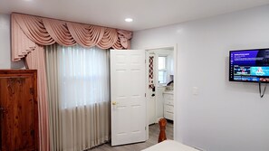 A room with a television mounted on the wall, a door with a curtain, and a wooden cabinet.