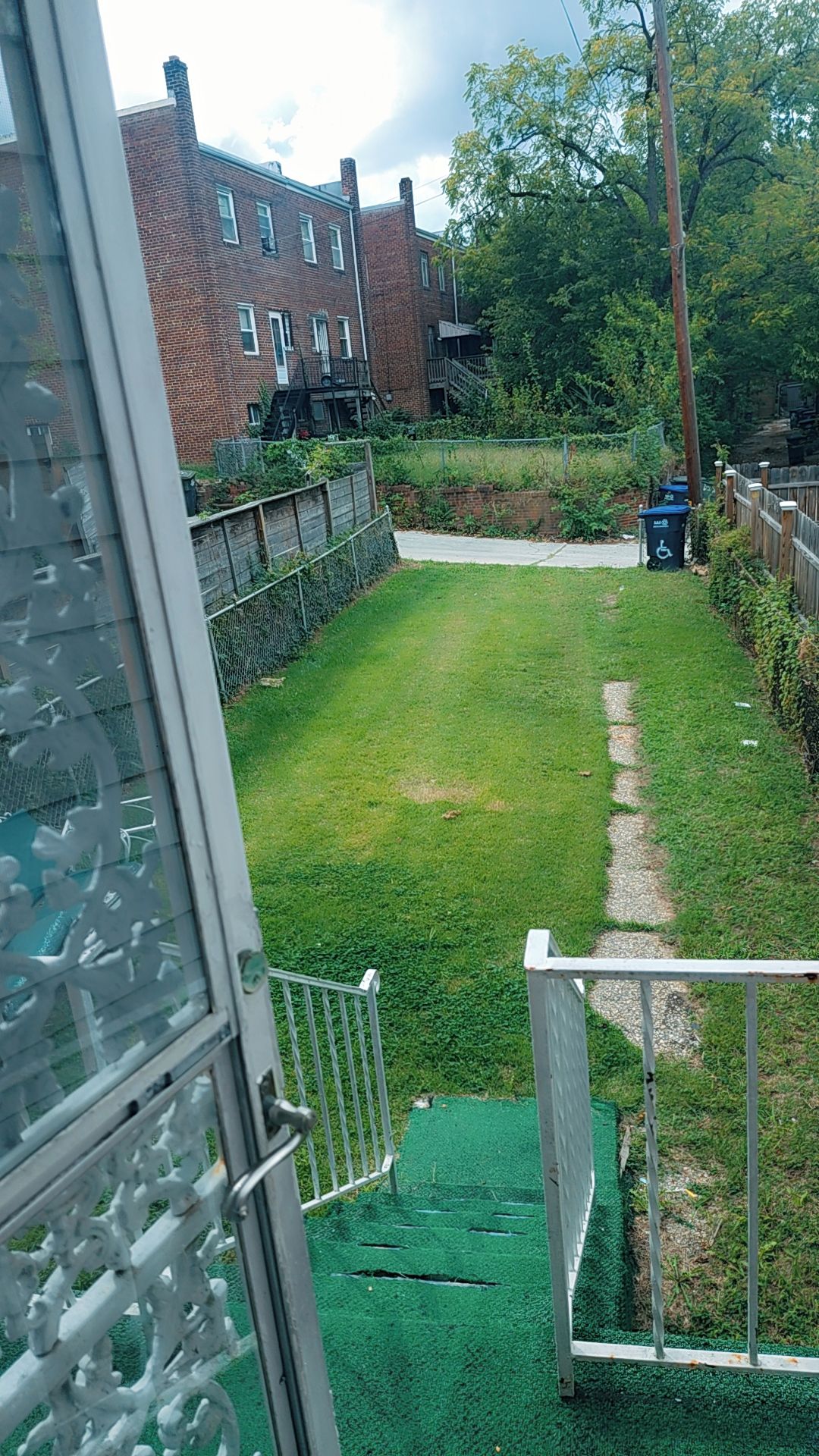 A residential backyard with a grassy lawn, a brick house, and a metal gate.