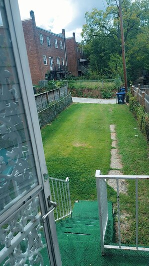 A residential backyard with a grassy lawn, a brick house, and a metal gate.