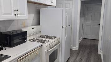 Una cucina con mobili bianchi, un fornello, un forno a microonde, un frigorifero e una lavastoviglie.