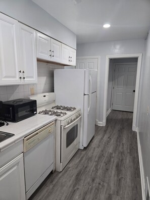 Una cocina con armarios blancos, estufa, microondas, refrigerador y lavavajillas.