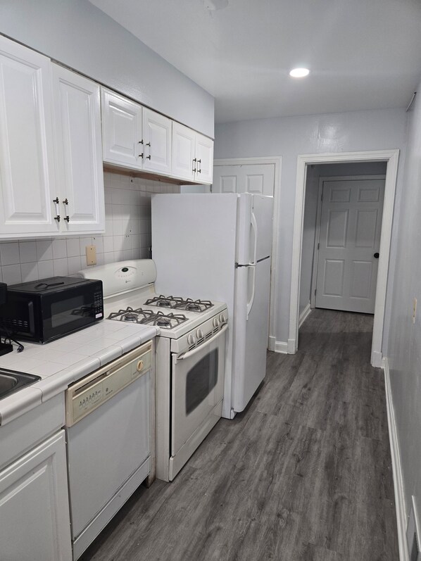A kitchen with white cabinets, a stove, a microwave, a refrigerator, and a dishwasher.