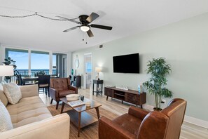 Uma sala de estar moderna com sofá, poltronas, mesa de centro, televisão e ventoinha de teto.