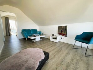 Un salon moderne avec un canapé turquoise, une table basse blanche, un pouf noir et un fauteuil turquoise.