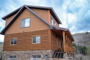 Una baita di legno con fondamenta in pietra, diverse finestre e un tetto spiovente.