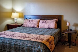 A bed with a patterned bedspread, two pillows with animal prints, a nightstand with a lamp, and a small table with another lamp. - Deer Creek Mountain Retreat (Heber City)