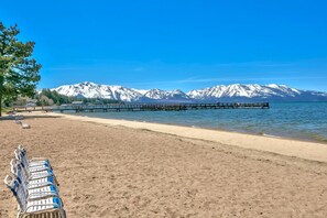 A beach with a wooden pier extending into calm waters, surrounded by snow-capped mountains. - LLV442 Lake and Mountain Retreat (South Lake Tahoe)