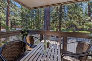 A wooden deck with wicker chairs and a table, overlooking a forested area with tall pine trees. - LLV442 Lake and Mountain Retreat (South Lake Tahoe)