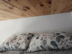 A room with a wooden ceiling, a bed with floral-patterned pillows, and a white striped wall.