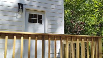 A wooden deck with a railing in front of a white house with a window and a door.