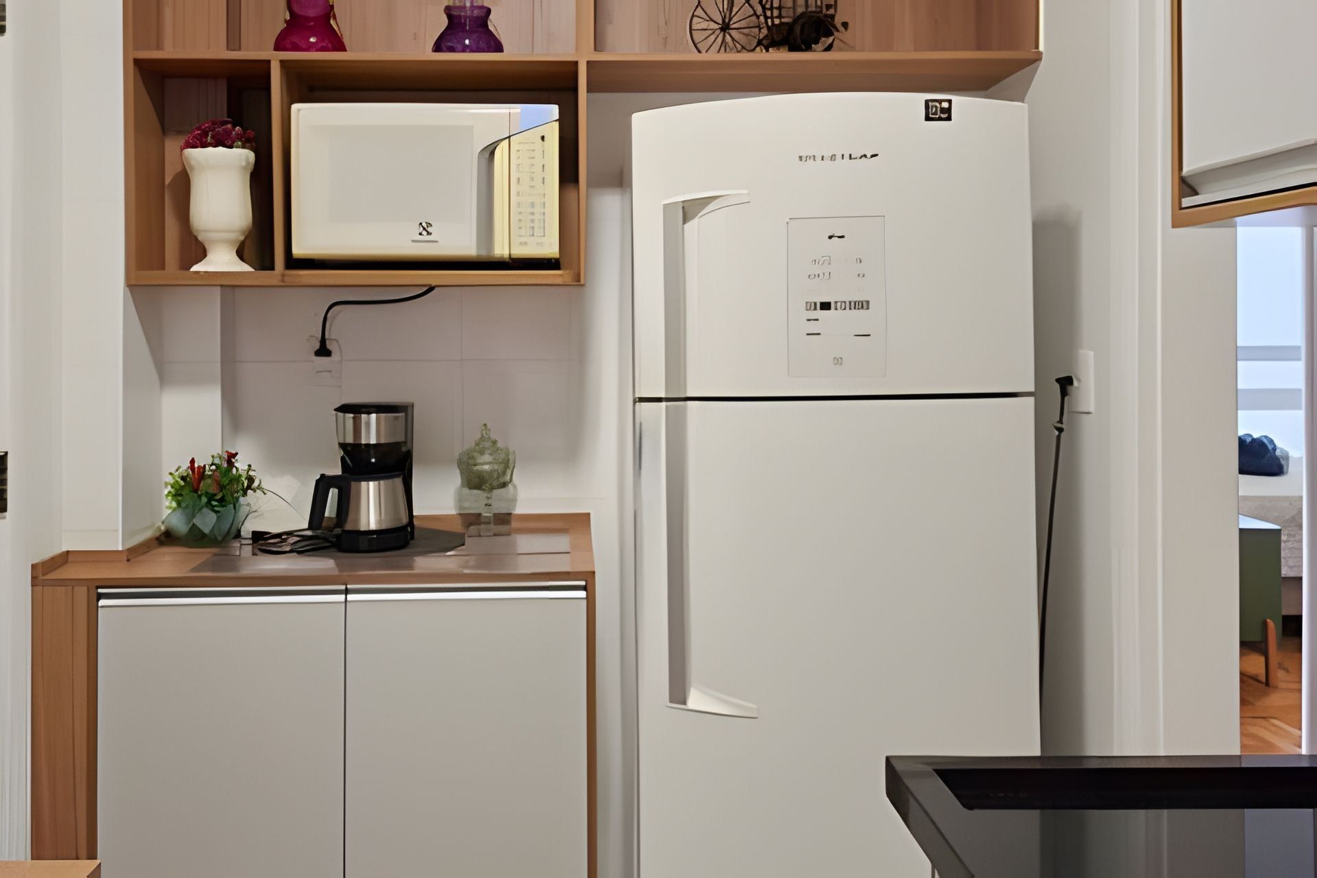 A kitchen with a white refrigerator, a microwave, a coffee maker, and a vase with flowers on the counter.