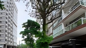 Uma rua com calçada arborizada, uma bicicleta estacionada e um prédio com loja.