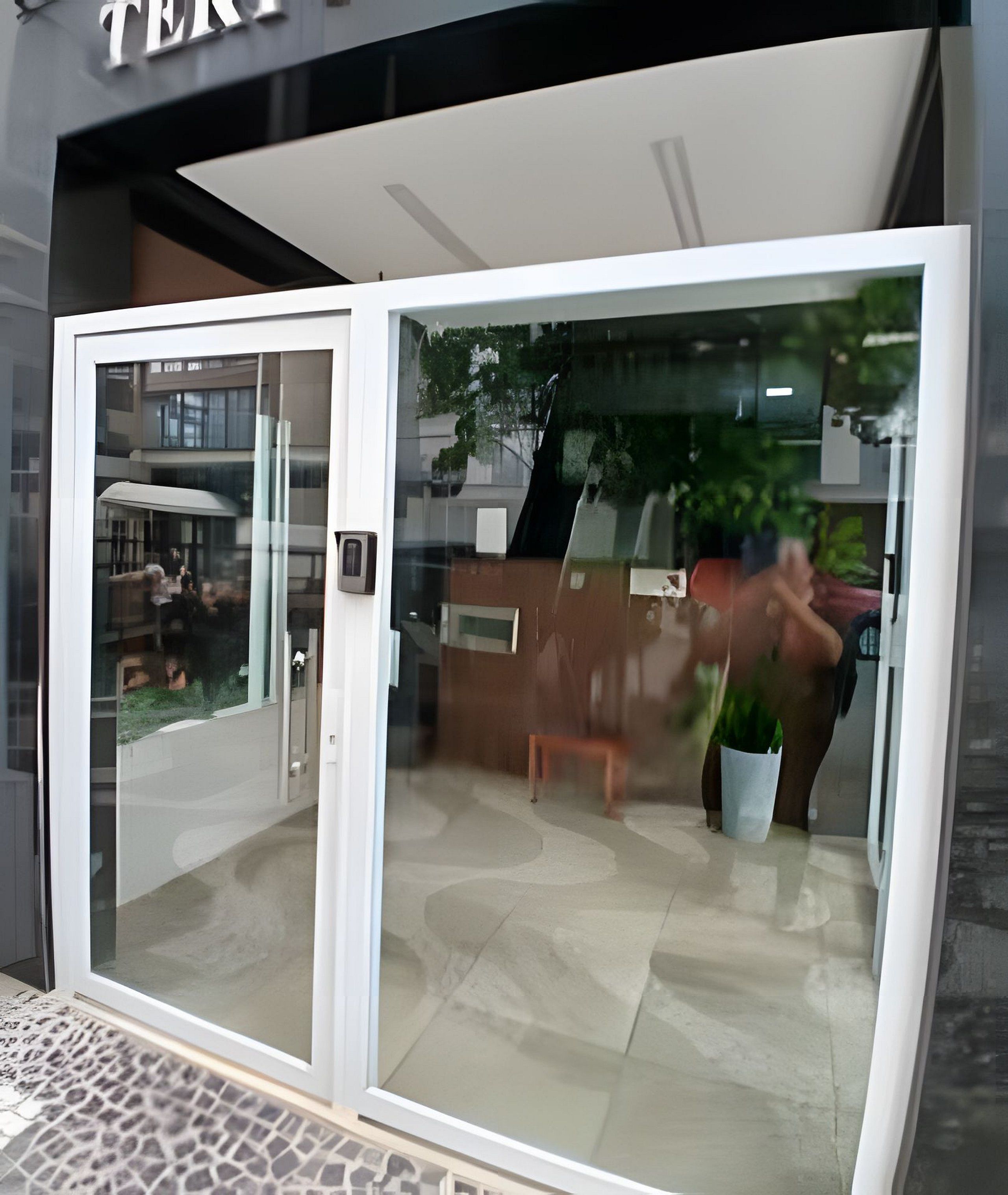 Entrada con puerta de vidrio que refleja un edificio y una persona.