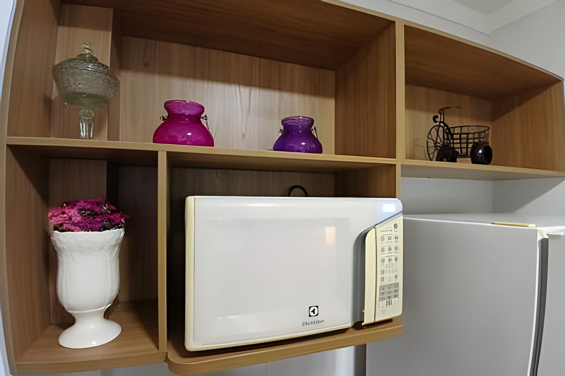 Une cuisine avec des étagères en bois, un micro-ondes blanc et un réfrigérateur blanc.