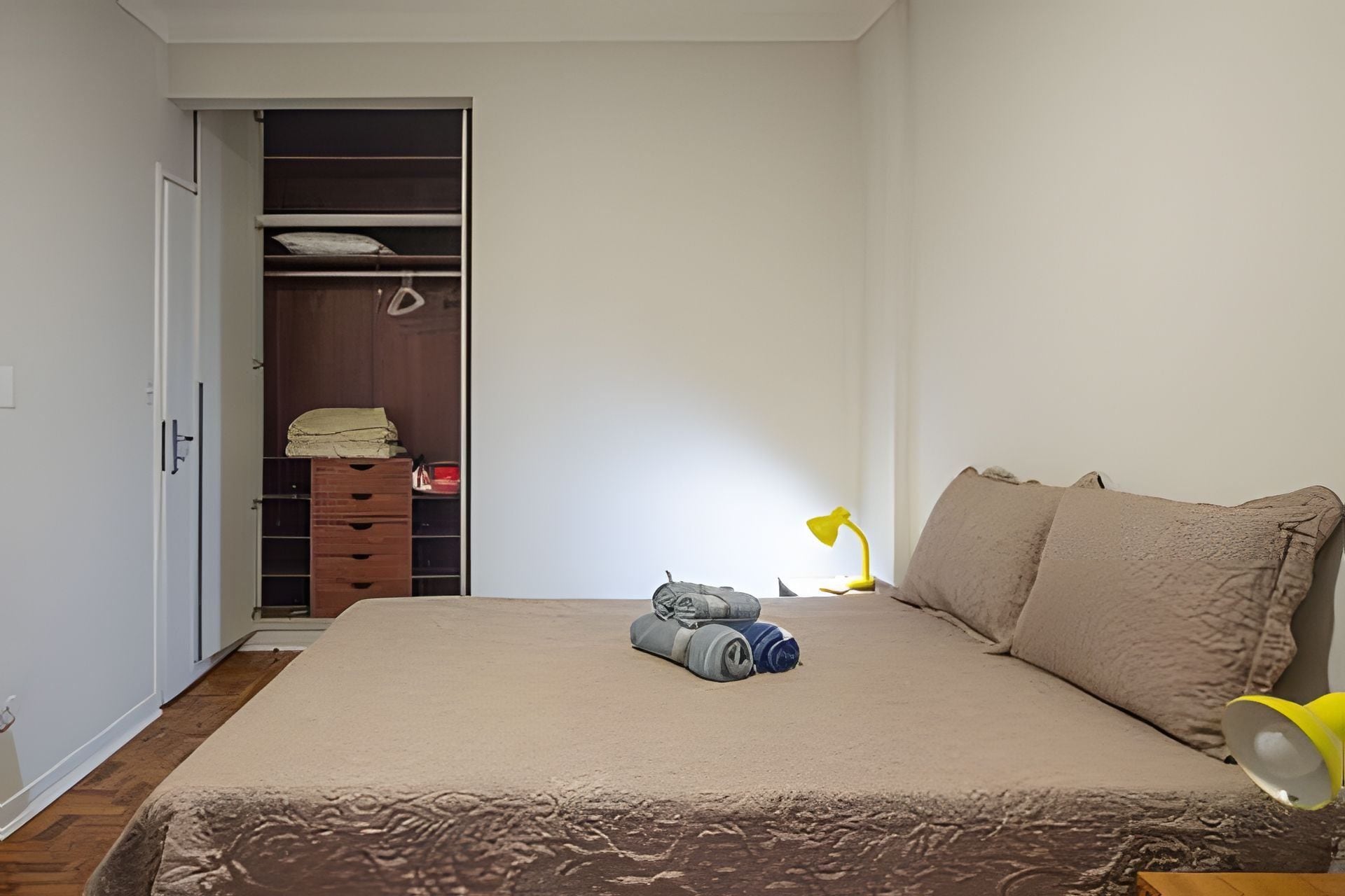 A bedroom with a bed, a bedside lamp, a wardrobe, and a small table with items on it.