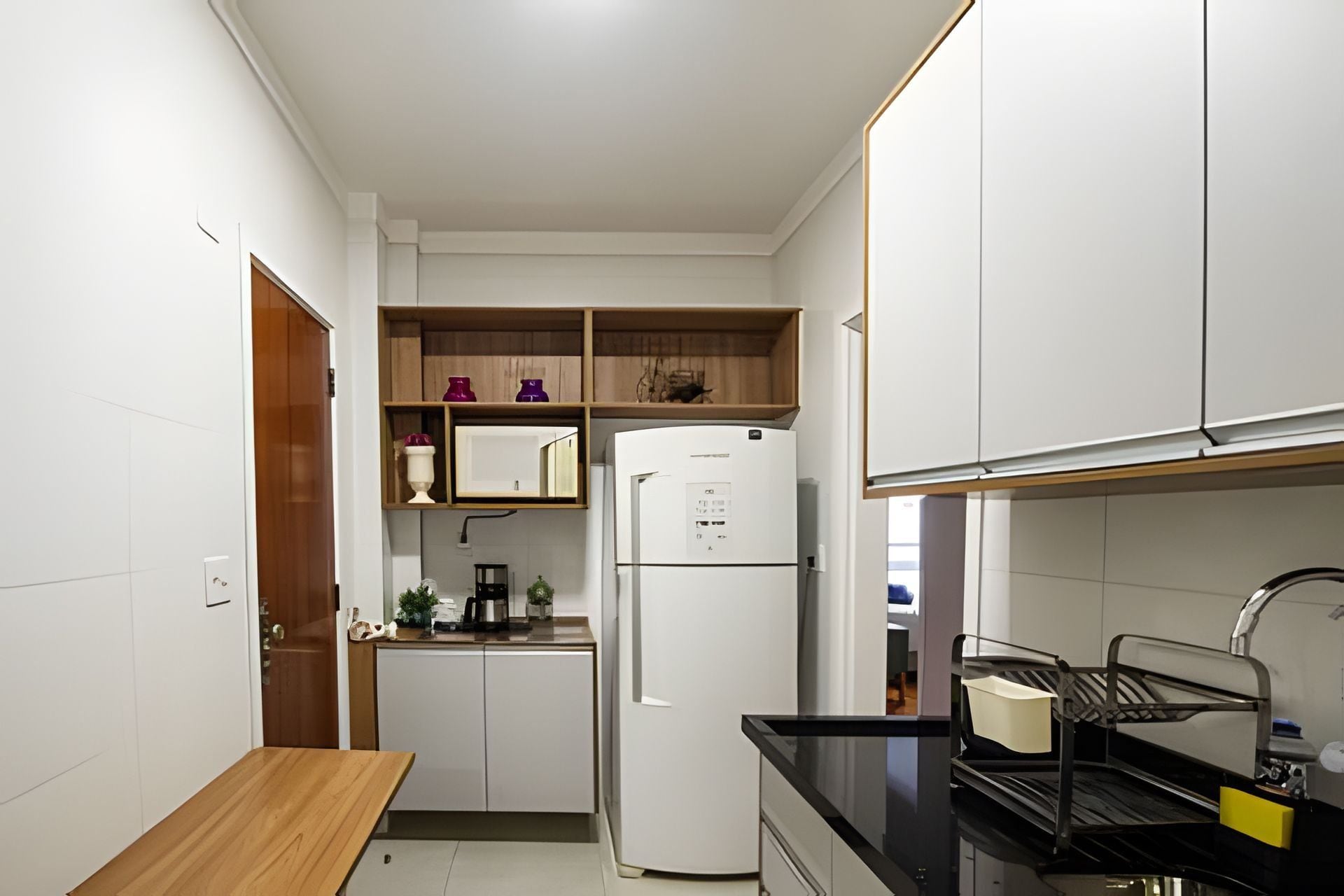 A compact kitchen with white cabinets, a white refrigerator, a wooden countertop, and a sink.