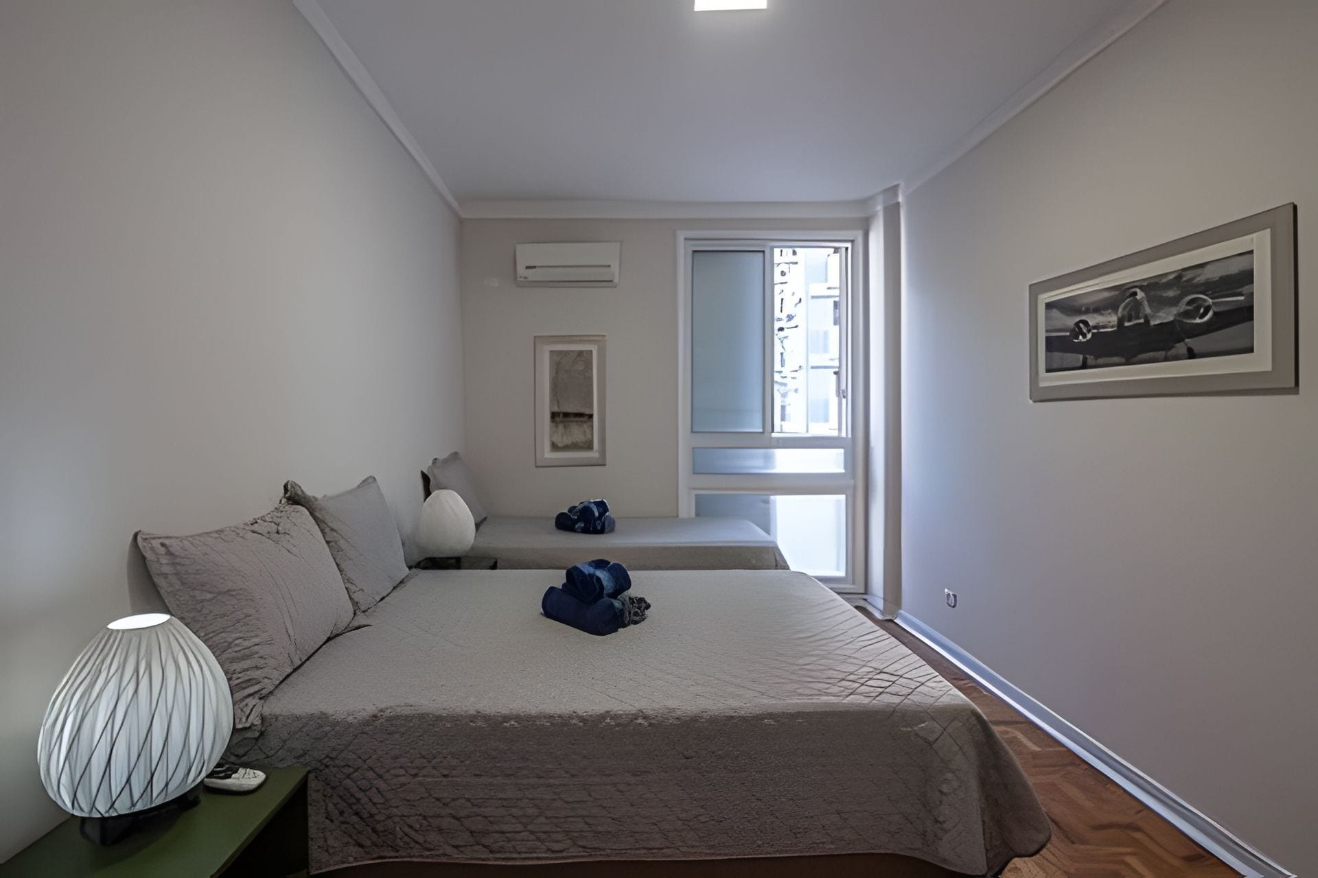 A bedroom with a bed, a nightstand, a lamp, a window, and a framed picture on the wall.