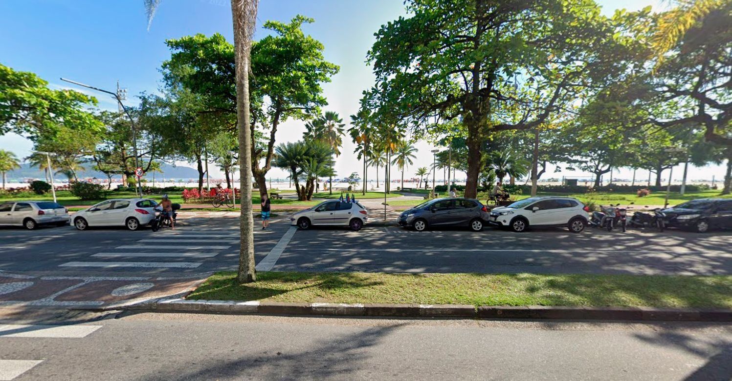 Une rue bordée de voitures garées et d’arbres, avec un passage piéton et une vue dégagée sur la route.
