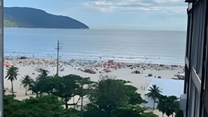 Vista costeira com uma praia, estrada com carros estacionados e um edifício em primeiro plano.