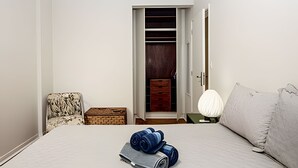Quarto com cama, mesa de cabeceira, cadeira, guarda-roupa e abajur.