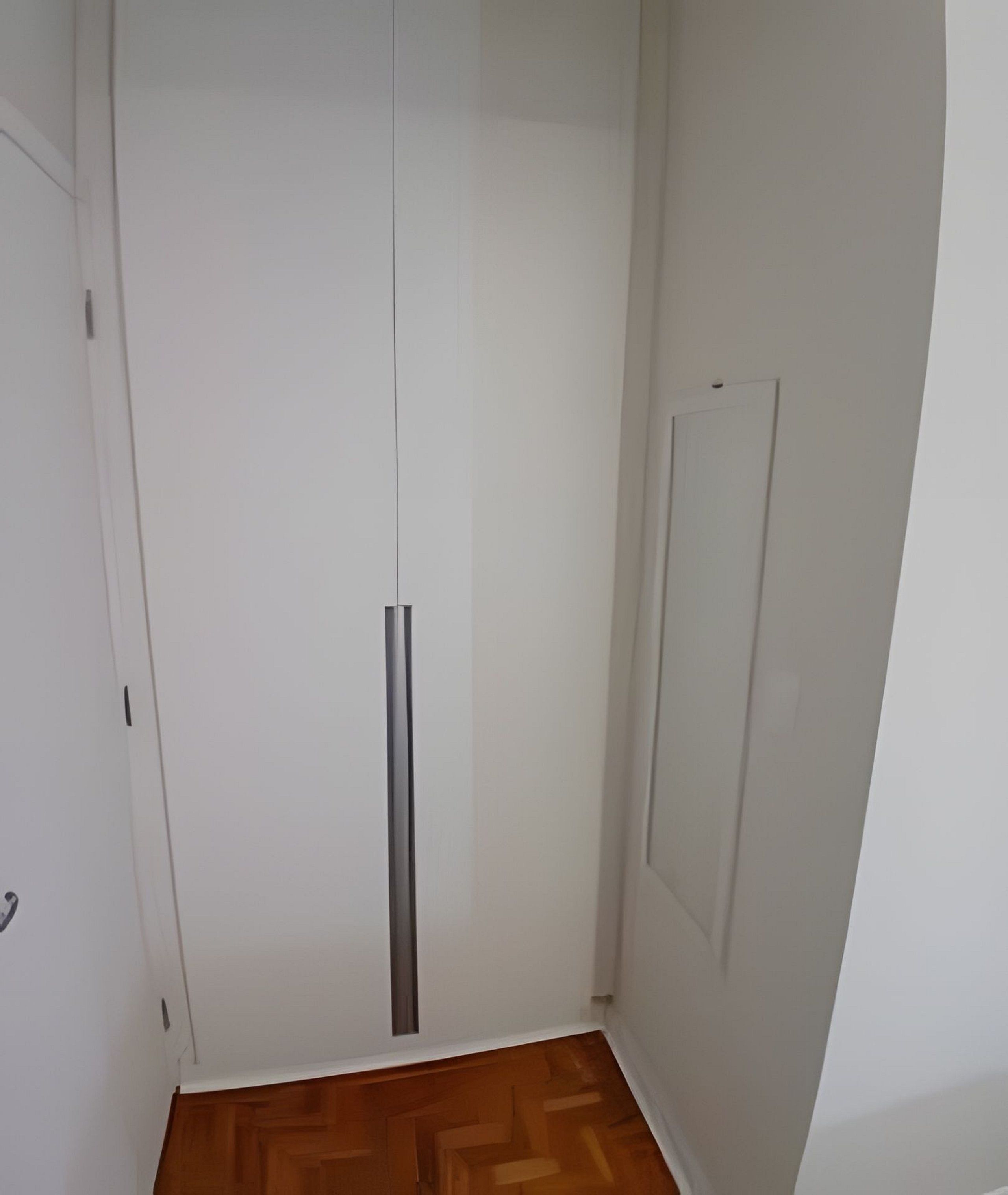A white wardrobe with a vertical handle, a wooden floor, and a white door with a small rectangular panel.
