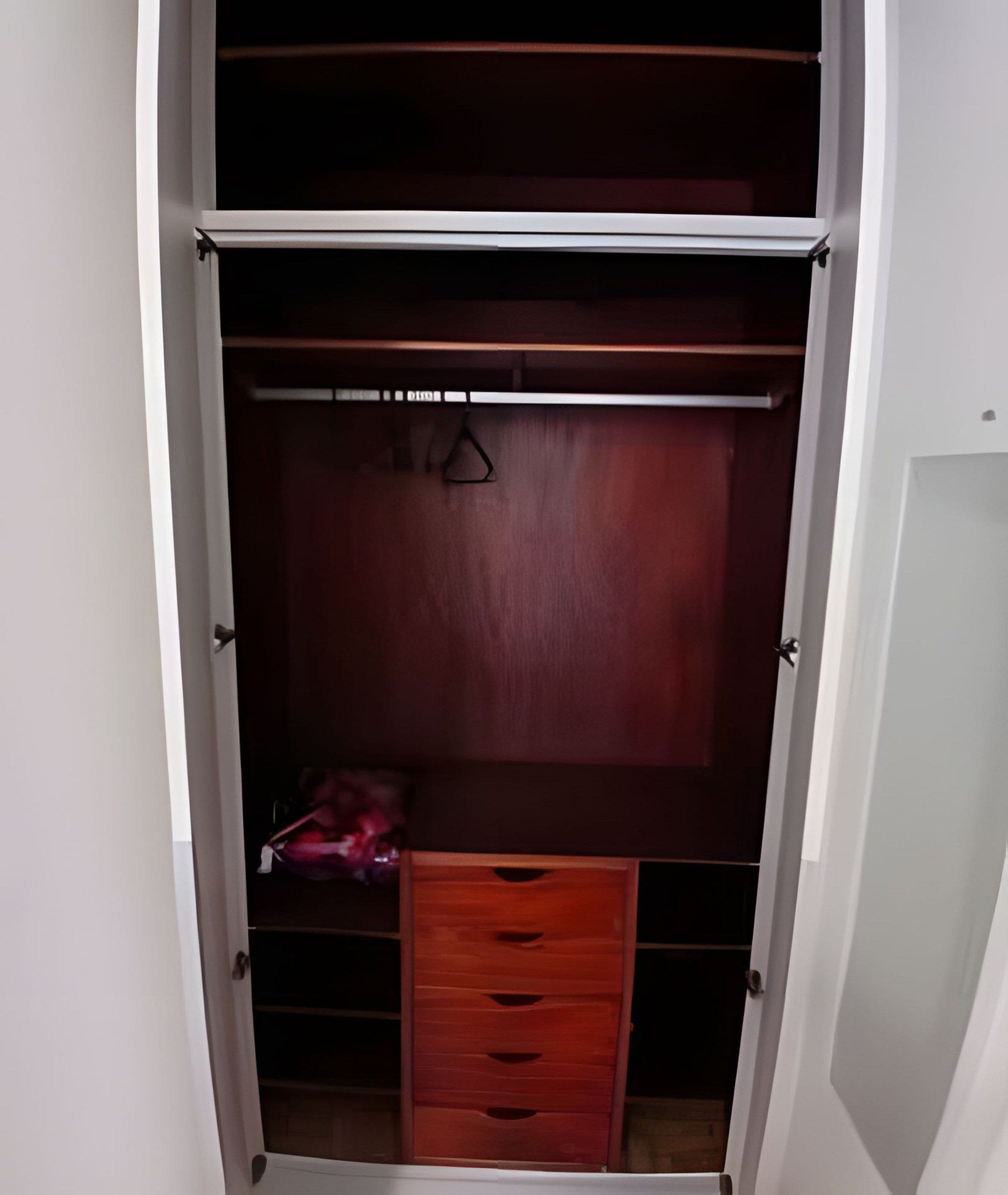 A walk-in closet with a wooden wardrobe, a hanging rack, and a small drawer unit.