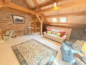 A cozy attic room with a wooden ceiling, a plaid sofa, a blue sofa, a patterned rug, and a brick wall with a framed picture. - Stone Fireplace + Game Room | 6 Min to Bromley | Sleeps 8–9 (Peru)
