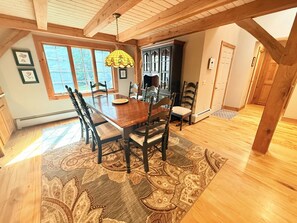 A dining area with a wooden table and chairs, a patterned rug, and a hanging lamp. - Stone Fireplace + Game Room | 6 Min to Bromley | Sleeps 8–9 (Peru)
