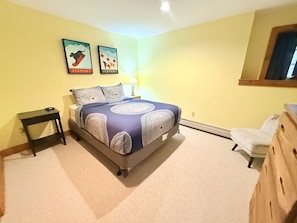 Ein Schlafzimmer mit einem Bett, einem Nachttisch, einer Kommode und zwei an der Wand hängenden Bildern.