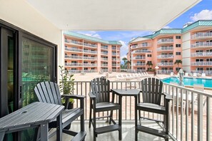 A balcony with outdoor seating and a view of a pool and hotel buildings. - Coastal Ocean View Condo at Beach Palms (Indian Shores)