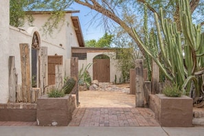 A rustic building with a brick pathway leading to a wooden door, surrounded by cacti and desert plants. - Tranquil Southwest Apt with Traditional Courtyard (Mesa)