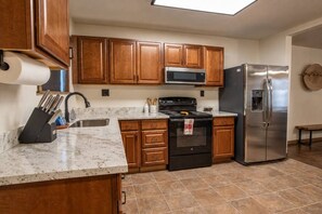 A kitchen with wooden cabinets, a stainless steel refrigerator, a microwave, and a stove. - Tranquil Southwest Apt with Traditional Courtyard (Mesa)