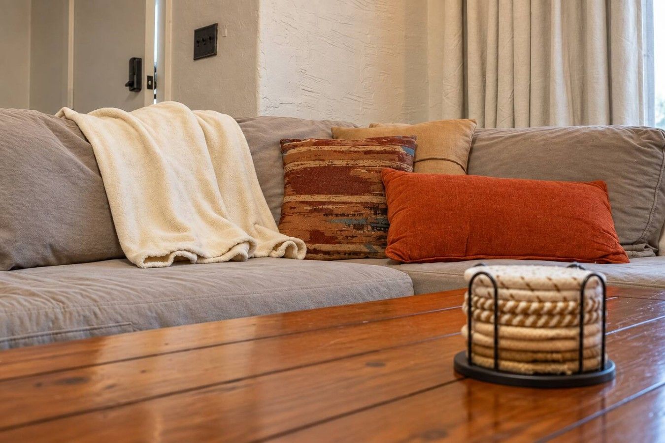 Un salon avec un canapé, un plaid, un coussin et une télécommande posés sur une table basse en bois.