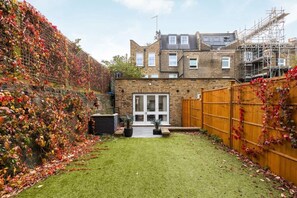 A residential property with a brick house, a wooden fence, and a garden with autumn leaves. - 2 Bed Private Garden near Shepherds Bush Westfield (London)