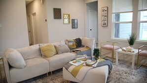 Un salon avec un canapé, une table basse et une fenêtre équipée de stores.