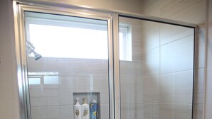 Une cabine de douche fermée par des parois en verre, avec un mur carrelé et une petite étagère contenant des articles de toilette.