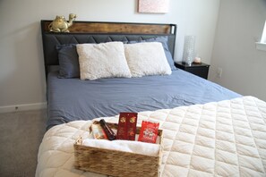 A neatly made bed with a dark blue bedspread, a white quilt, and a basket containing toiletries.