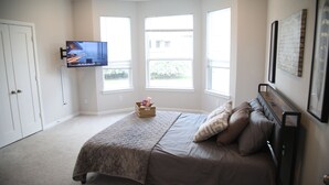 Une chambre à coucher avec un lit, un téléviseur fixé au mur et de grandes fenêtres.