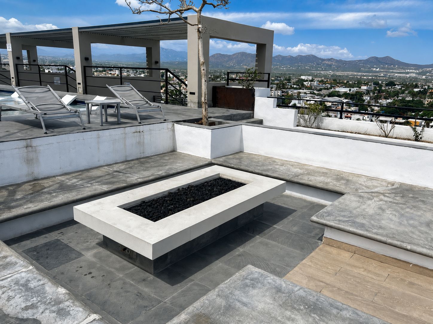 Une terrasse sur le toit avec un foyer, des chaises longues et une vue sur la ville et les montagnes.