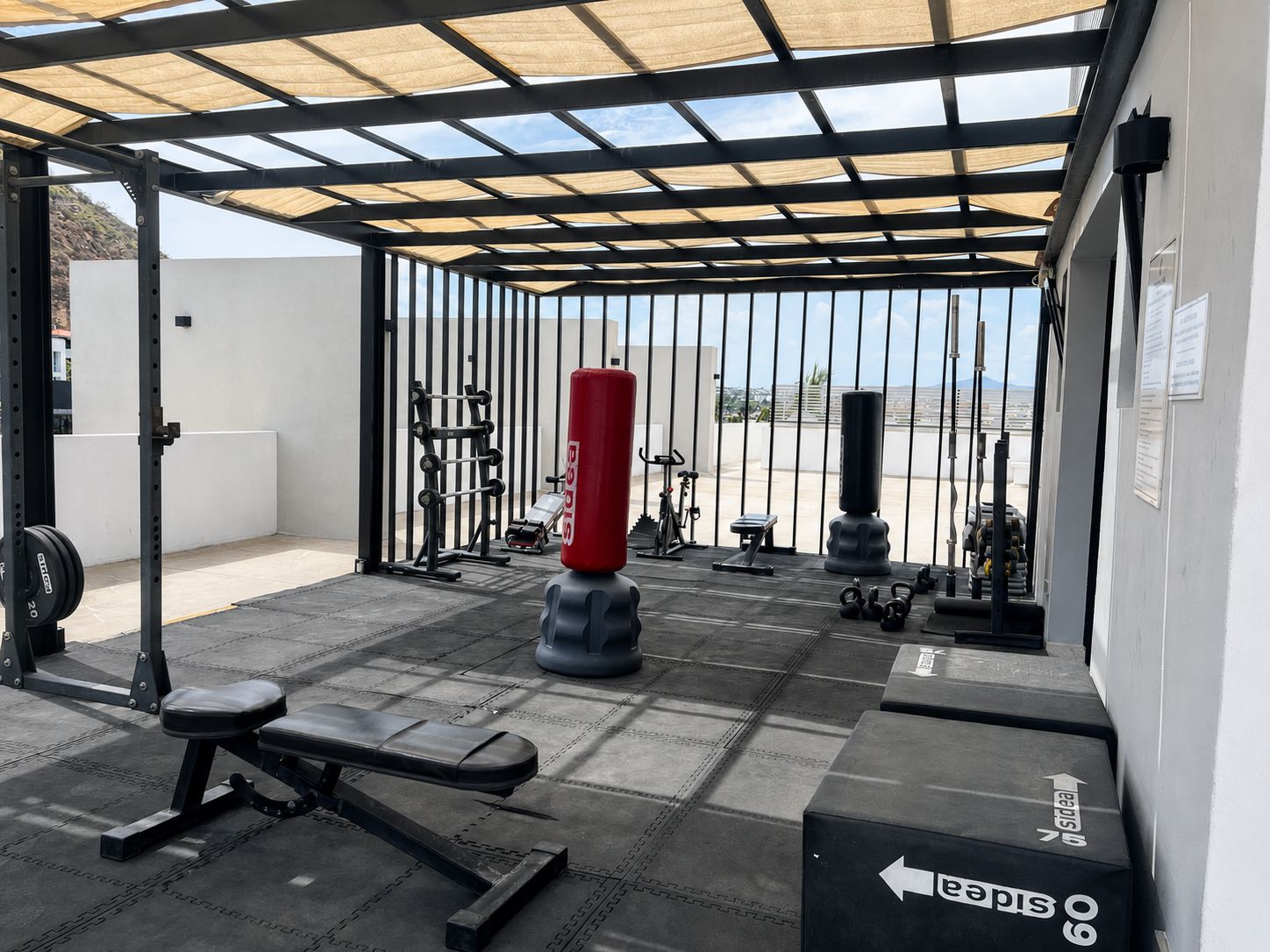 Un espace de remise en forme extérieur abrité, équipé de matériel d’exercice, notamment un banc, des haltères et un sac de frappe.