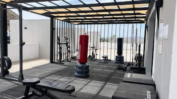 Un espace de remise en forme extérieur abrité, équipé de matériel d’exercice, notamment un banc, des haltères et un sac de frappe.